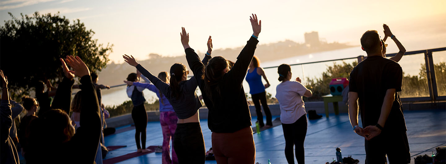 Yoga practitioners stretch their arms toward the sky in a group class -- silhouetted against a sunset sky