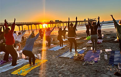 Students doing yoga on the sand near Scripps Pier - with a glorious glowing sun setting over the ocean behind them